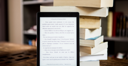 An eBook on a tablet standing against a pile of books.