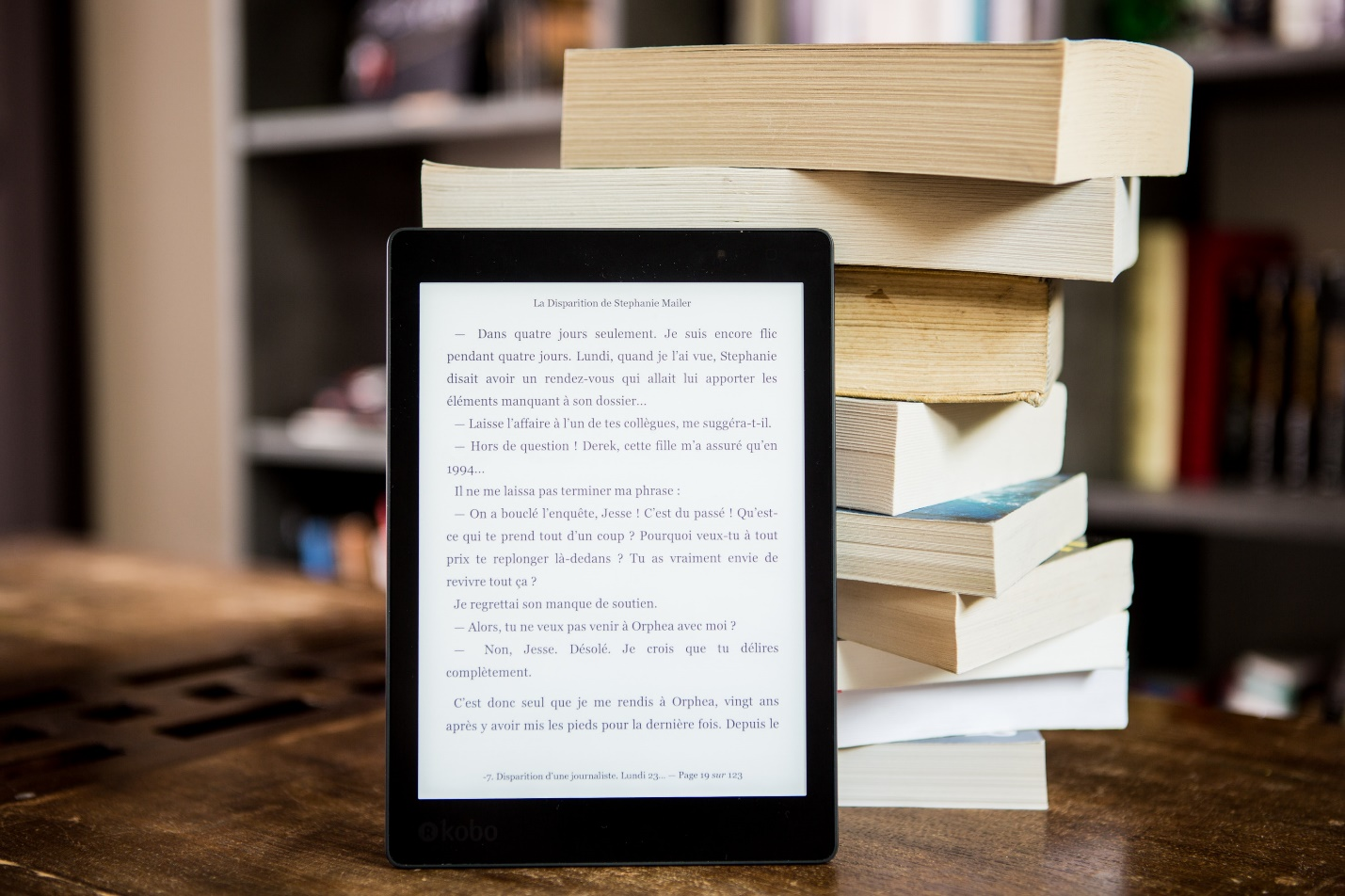 An eBook on a tablet standing against a pile of books.
