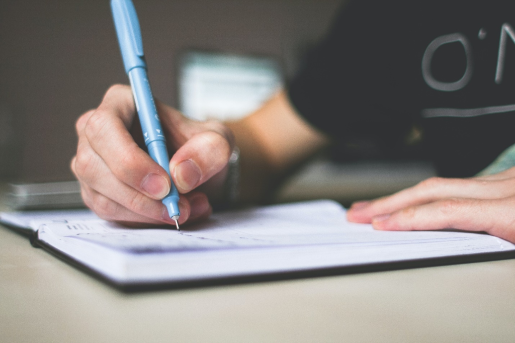 A person writing in a notebook with a pen. 