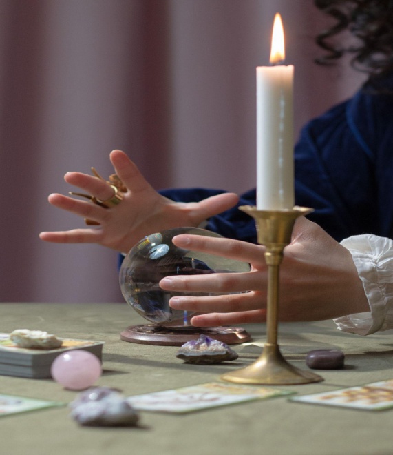 a fortune teller's hands hovering over a crystal ball on table.