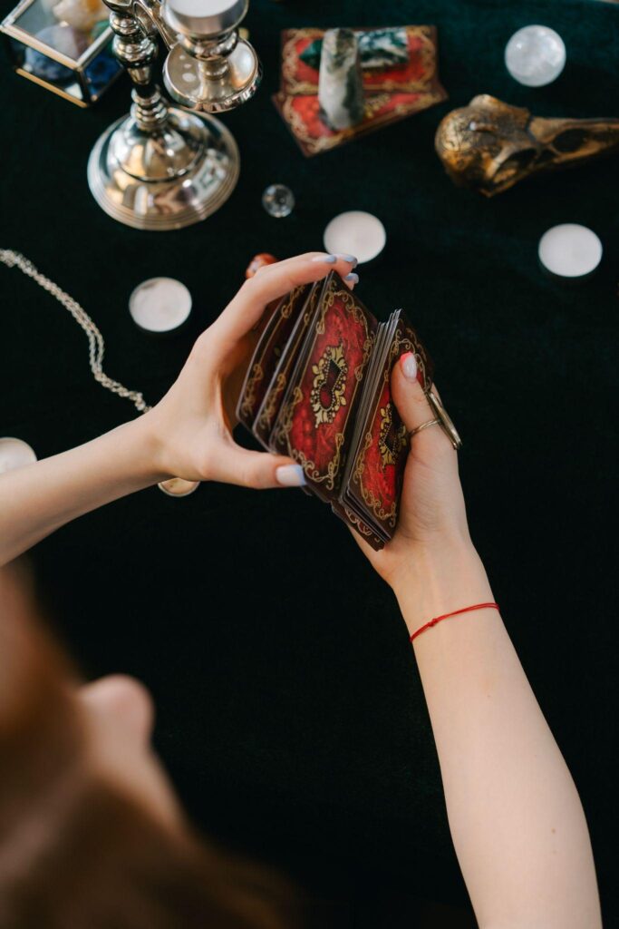 Overhead image of a person’s arms as they shuffle a tarot card deck. Metallic ornaments and decoration are visible on the black table below